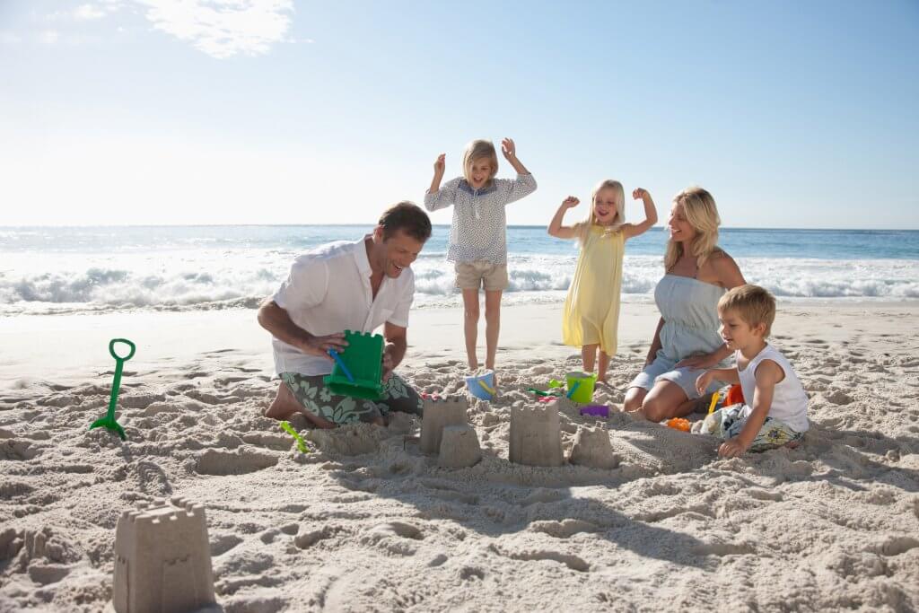 Family making a sandcastle in the sand with water in the background