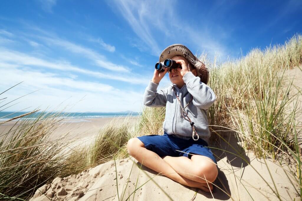 Little boy searching with binoculars at the beach dressed as explorer concept for nature, discovery, exploring and education
